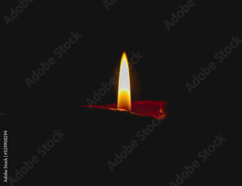 One candle burning brightly on a black background. A red candle burns on a dark background. The candle flame is isolated on a black background.