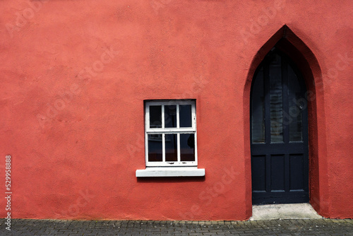 Red color wall and wooden old style black door and white wooden window. Copy space. Exterior of an antique style building. Rich saturated color. © mark_gusev