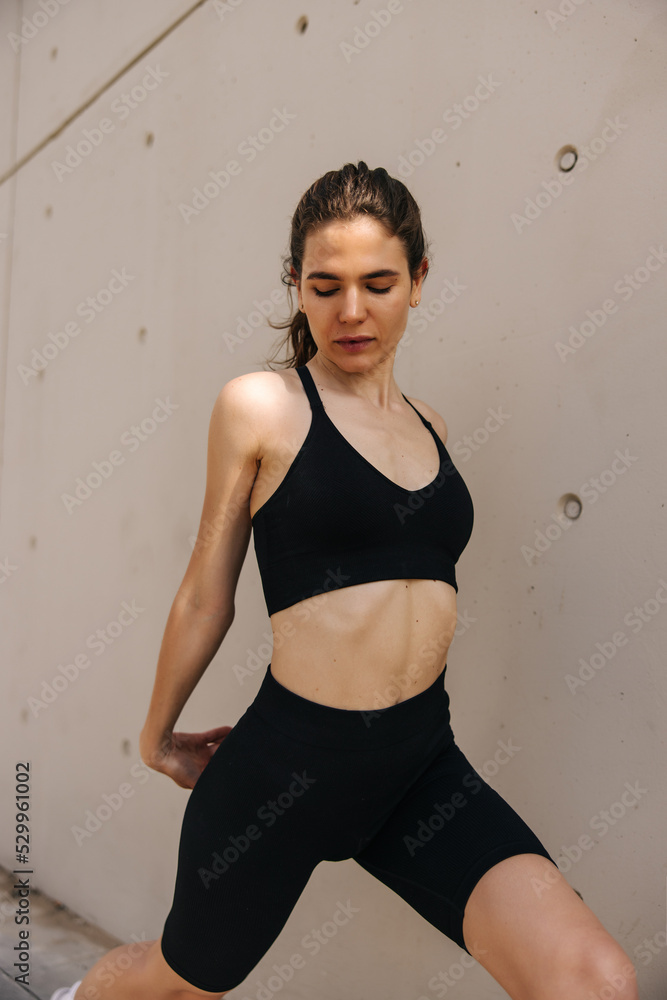 Attractive slim woman looking down keep hands together and doing exercise. Staying near to wall in black sportswear, have stretching for arms. Concept of outdoors workout Attractive slim woman looking down keep hands together and doing exercise. Staying near to wall in black sportswear, have stretching for arms. Concept of outdoors workout