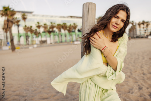 Beautiful dark-haired pretty woman keep hands crossed at beach. Looking to camera on the palms background. Concept of chilling mood outdoors 