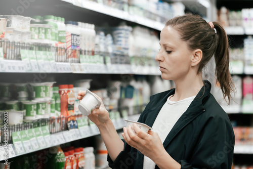Schilderij op canvas a young lady in the store chooses yogurt products, reads and compares the composition on the labels