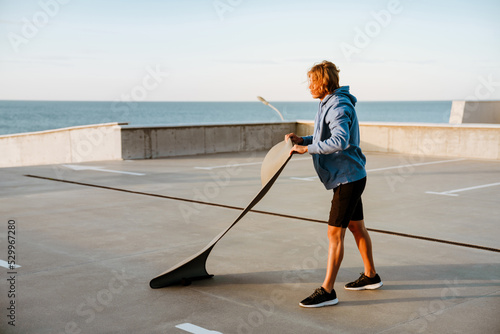 Young blonde man working out with fitness mat on parking