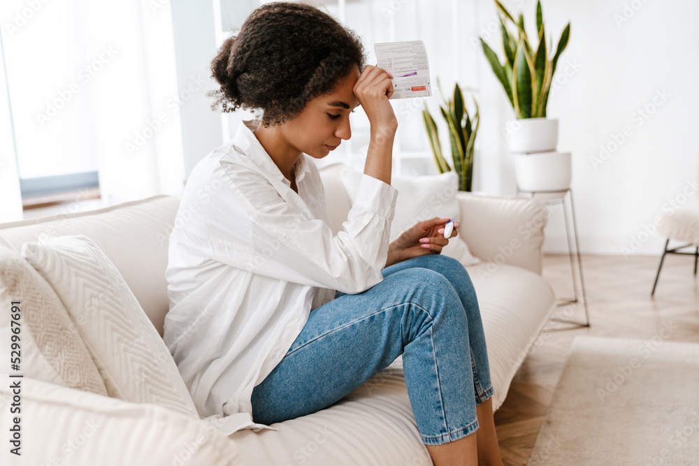 Young black woman being upset while holding pregnancy test at home Young black woman being upset while holding pregnancy test at home