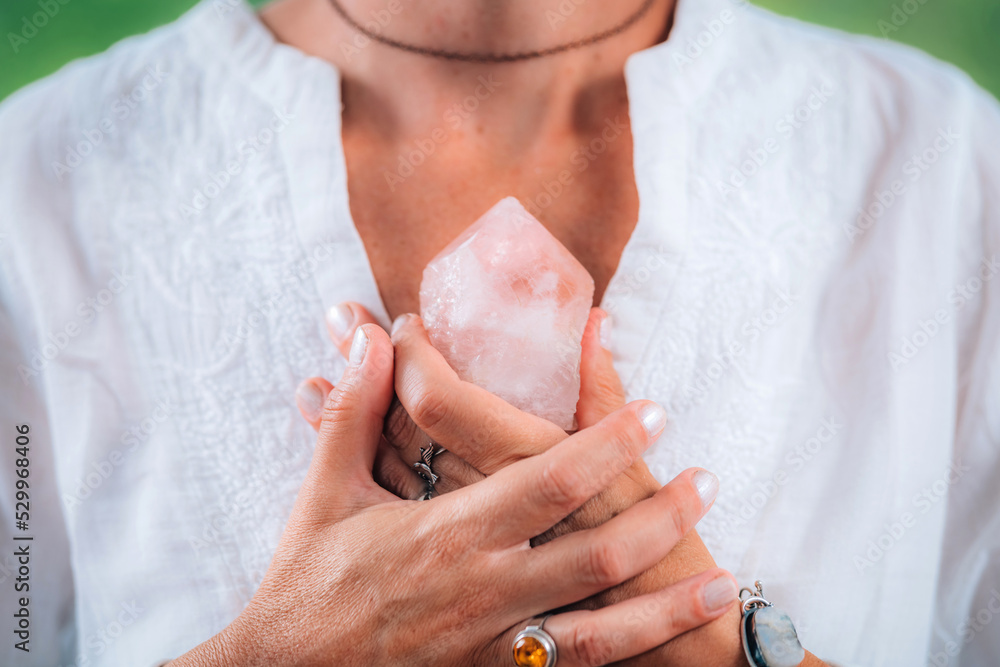 Self-worth meditation concept. Hands holding a rose quartz crystal, meditating, improving a sense of self-worth, focusing on being good and worthy of love and belonging - obrazy, fototapety, plakaty 