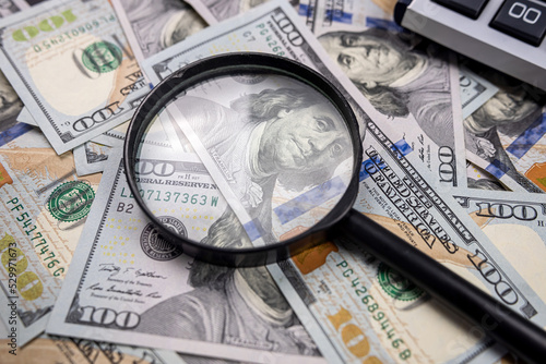 magnifying glass on pile of US dollar money banknotes with calculator isolated on wooden table