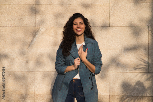 Beautiful young woman with curly brown hair and upturned nose dressed in fashionable clothes poses for photos as a super model on a brown background. Concept of beauty and fashion. photo