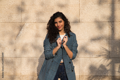 Beautiful young woman with curly brown hair and upturned nose dressed in fashionable clothes poses for photos as a super model on a brown background. Concept of beauty and fashion.