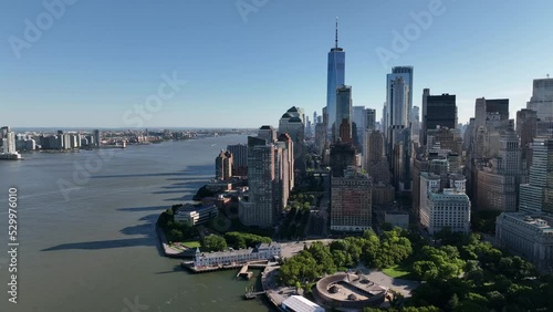 An aerial view of Manhattan and New York Harbor on a sunny day with blue skies. The drone camera facing lower Manhattan truck left and pan right over the calm waters.