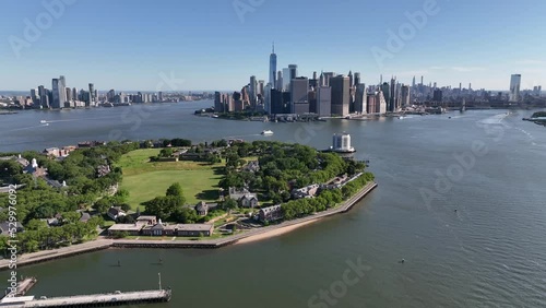 An aerial view of New York harbor on a sunny day with clear blue skies. The drone camera dolly out from lower Manhattan, high up over the water, passing above Governors Island. photo