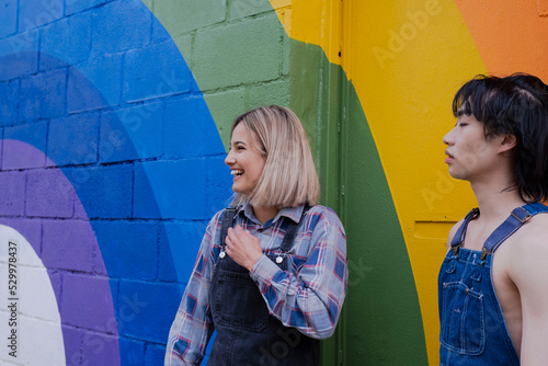 Happy young woman standing by friend in front of rainbow mural photo