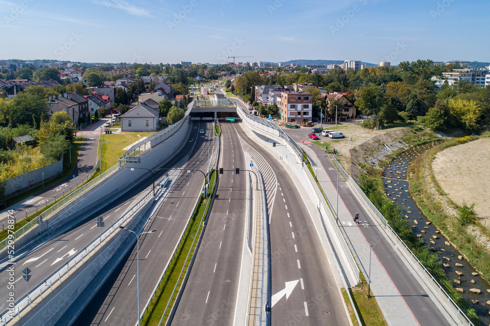 Fototapeta premium New city highway Trasa Lagiewnicka in Krakow, Poland, with tunnels, slip ways, cycle path and pavement for pedestrians. Regulated Wilga river decorated with stones