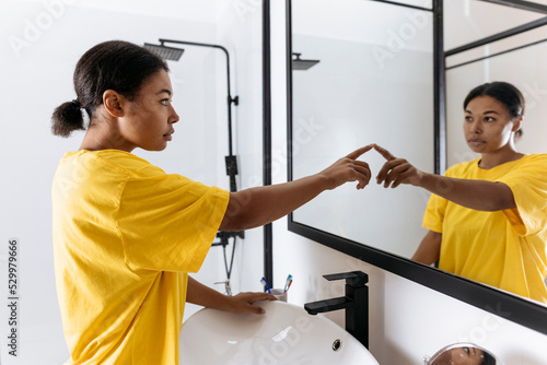 Woman pointing at herself in bathroom mirror photo