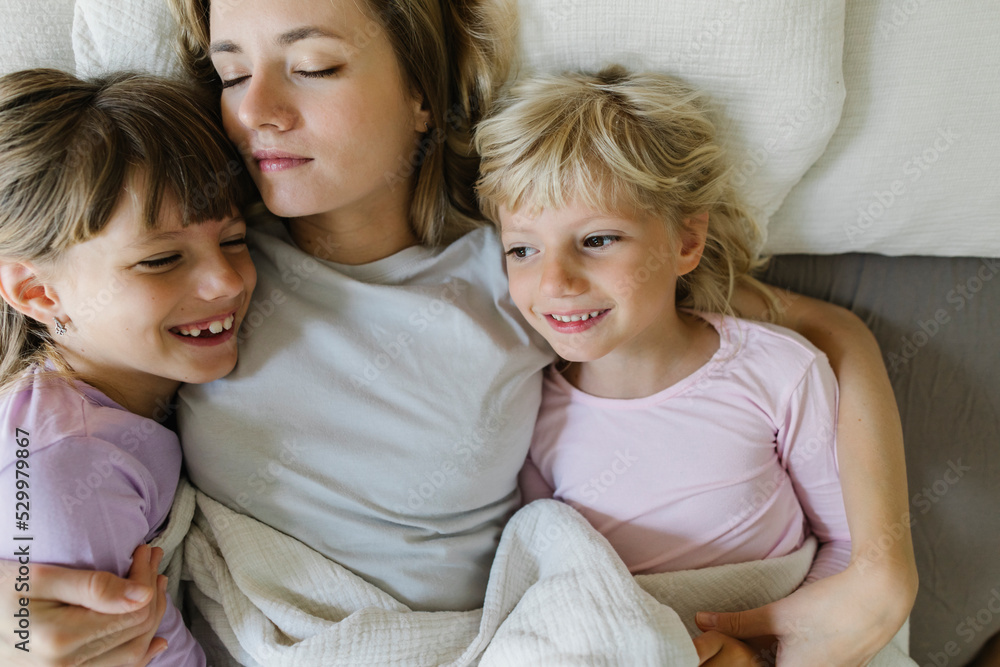 Smiling siblings relaxing with mother in bed at home Smiling siblings relaxing with mother in bed at home