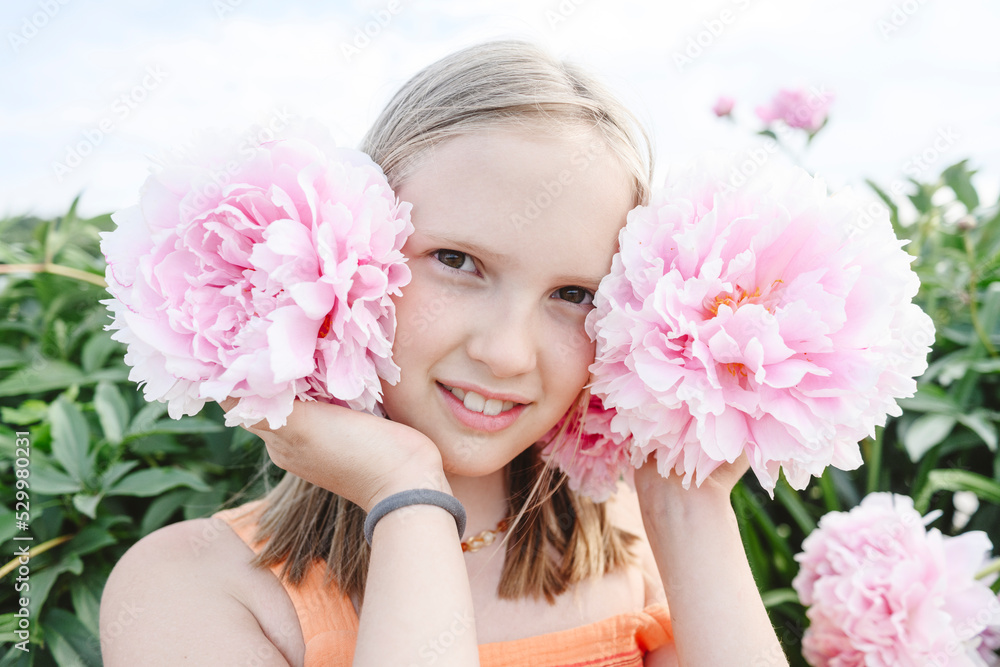 Smiling blond girl holding pink peony flowers Smiling blond girl holding pink peony flowers