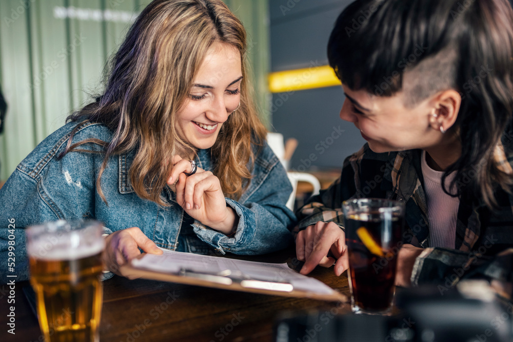 Happy lesbian couple with food menu sitting at table in restaurant