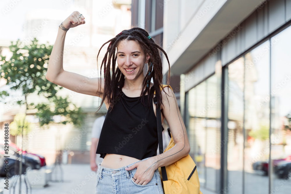 Smiling non-binary person with hand in pocket flexing muscle Smiling non-binary person with hand in pocket flexing muscle