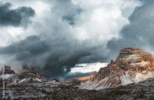 Mystical beautiful mountain landscape with a house on top of a mountain and church with thunder clouds and fog in cloudy weather. Tre Cime park in Dolomites, Italy. Italian alps