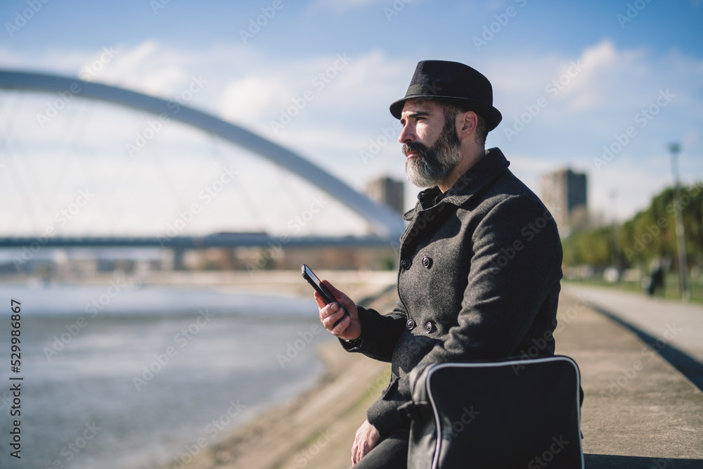 Obraz premium Businessman is sitting outdoor in the city and using smartphone.