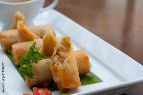 Tasty fried spring rolls and sauce on wooden table against blurred background