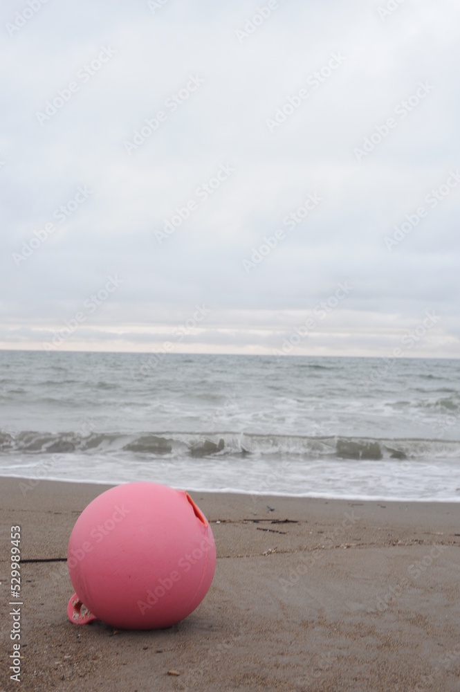 Pink buoy stranded on a sand beach on a grey cloudy day at the seaside with clear horizon on the shore Pink buoy stranded on a sand beach on a grey cloudy day at the seaside with clear horizon on the shore