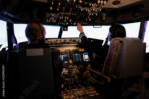 Woman copilot assisting captain to takeoff and fly airplane, using buttons on dashboard command in pilot cockpit. Airliners flying plane jet with navigation windscreen and control panel. photo