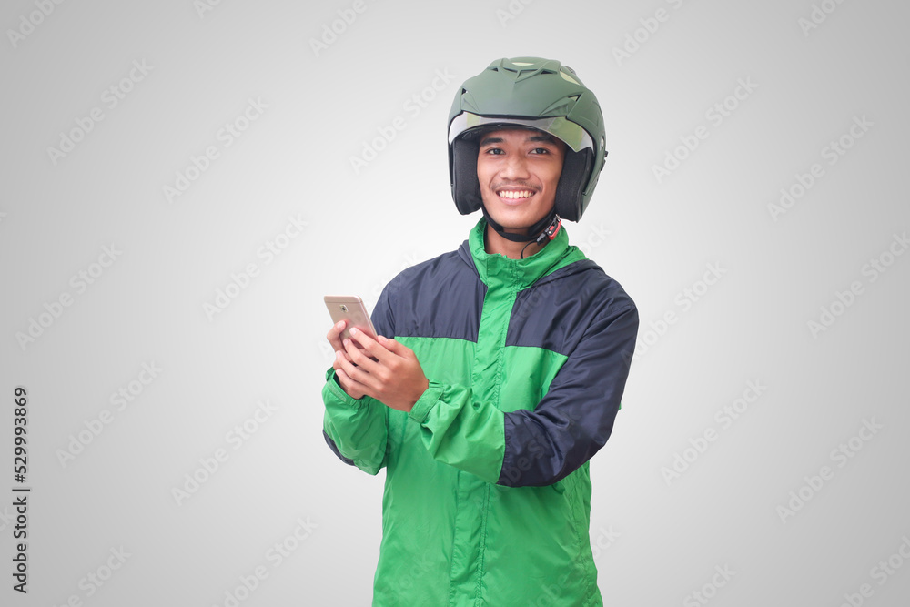 Portrait of Asian online taxi driver wearing green jacket and helmet holding a mobile phone and smiling. Advertising concept. Isolated image on white background Portrait of Asian online taxi driver wearing green jacket and helmet holding a mobile phone and smiling. Advertising concept. Isolated image on white background