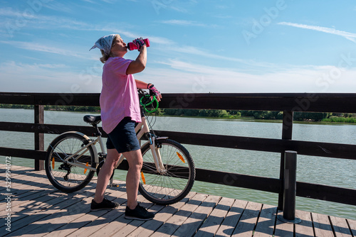 Woman athlete drinks water from a plastic bottle. Quenching thirst. Restoration of trace elements of the body, water-salt balance. Cycling in the park area.