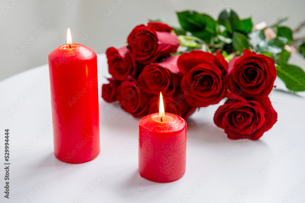 Romantic still life, there are two red burning candles and a bouquet of roses on the table Romantic still life, there are two red burning candles and a bouquet of roses on the table