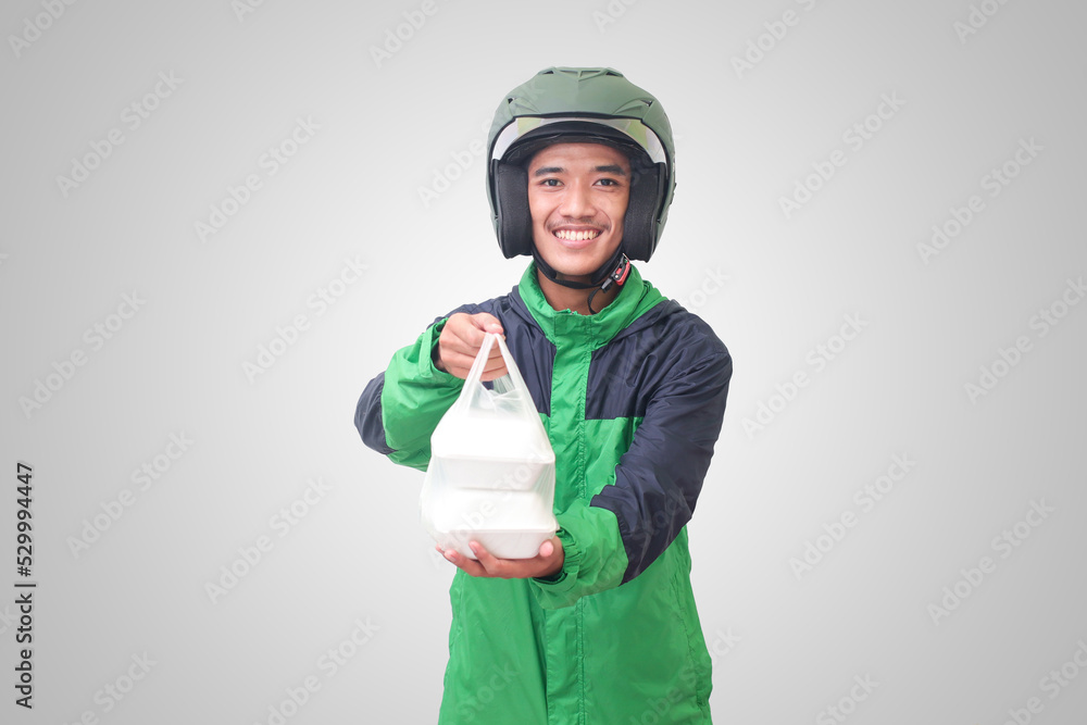 Portrait of Asian online taxi driver wearing green jacket and helmet holding food wrapped in foam plastic box. Isolated image on white background Portrait of Asian online taxi driver wearing green jacket and helmet holding food wrapped in foam plastic box. Isolated image on white background