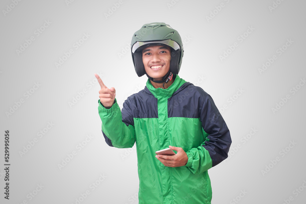 Portrait of Asian online taxi driver wearing green jacket and helmet holding mobile phone and pointing to empty space with finger. Isolated image on white background Portrait of Asian online taxi driver wearing green jacket and helmet holding mobile phone and pointing to empty space with finger. Isolated image on white background