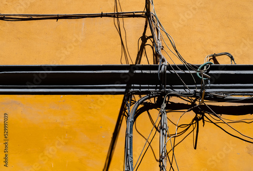 Yellow wall facade with wires  cabling and electric installations for power supply of city houses lit by bright sunlight in Naples  Itlay. Background with high contrast and crossing lines.