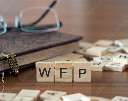 the acronym wfp for world food programme word or concept represented by wooden letter tiles on a wooden table with glasses and a book