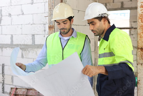 Two technician civil engineer or specialist inspector discussing, brainstorm and planing work with laptop, blueprint and walkie talkie radio together at Industrial building site. Construction concept