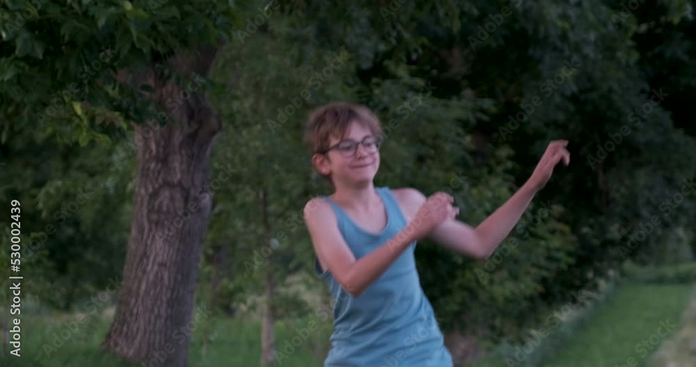 Cheerful boy jumps and spins waving his arms on deciduous trees background. Child games outside in forest. Cheerful boy jumps and spins waving his arms on deciduous trees background. Child games outside in forest.