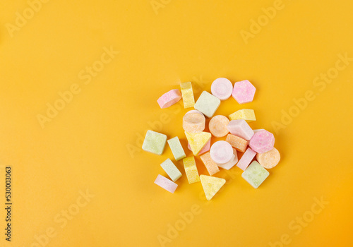 Tablet candies on yellow background. Compressed sugar powder confectionery, dextrose candy necklace parts, vitamin c tablets, lozenges pile top view photo