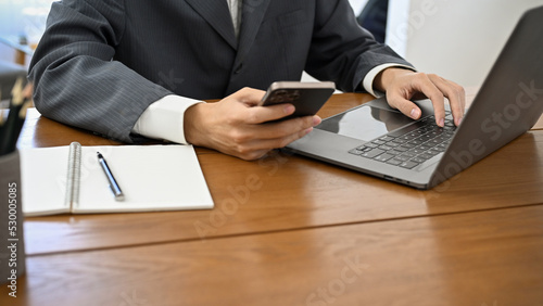 Businessman, lawyer or consultant working at his office desk, using smartphone and laptop