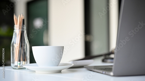 Modern white office desk workspace with notebook laptop, a coffee cup and office supplies