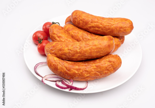 Smoked pork sausage on a white plate, isolated. Polish meat sausage, horizontal view.