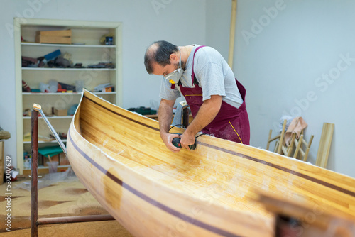Young carpenter making wooden boat in his carpentry workshop 