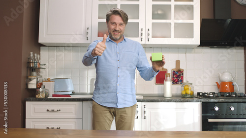 Fotografía A young man is holding something green in the kitchen, showing a product, smiling and presenting a cheerful, imaginary object