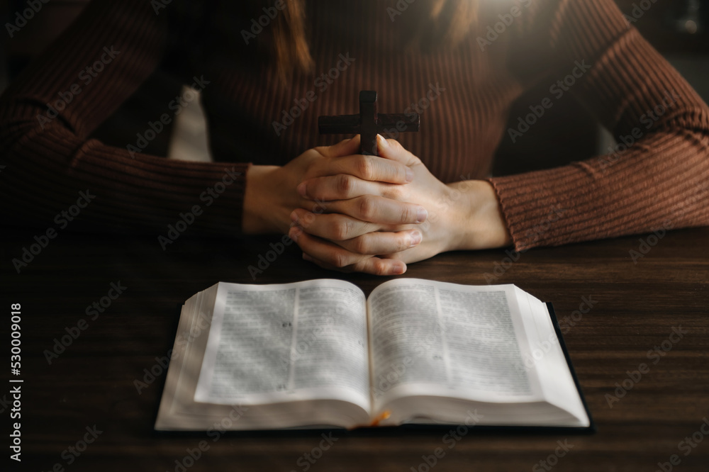 Hands together in prayer to God along with the bible In the Christian concept and religion, woman pray in the Bible on the wooden table