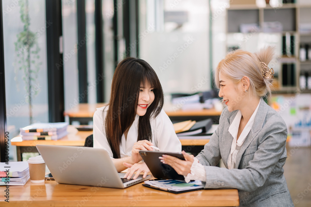 Two Asian businesswoman discuss investment project working and planning strategy with tablet laptop computer in modern office.. Two Asian businesswoman discuss investment project working and planning strategy with tablet laptop computer in modern office..