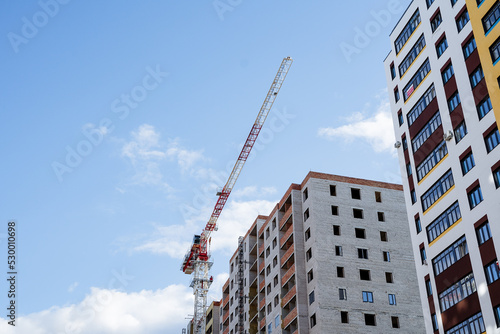 A construction crane against the background of a multi-storey building, a construction site, the construction of a residential building, a long boom of a crane.