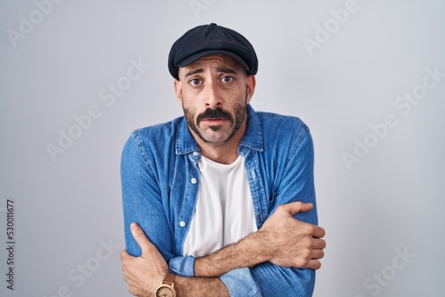 Hispanic man with beard standing over isolated background shaking and freezing for winter cold with sad and shock expression on face