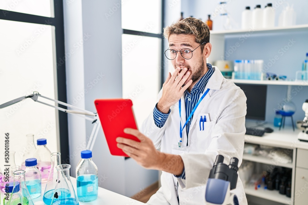 Hispanic man with beard working at scientist laboratory doing video call covering mouth with hand, shocked and afraid for mistake. surprised expression Hispanic man with beard working at scientist laboratory doing video call covering mouth with hand, shocked and afraid for mistake. surprised expression