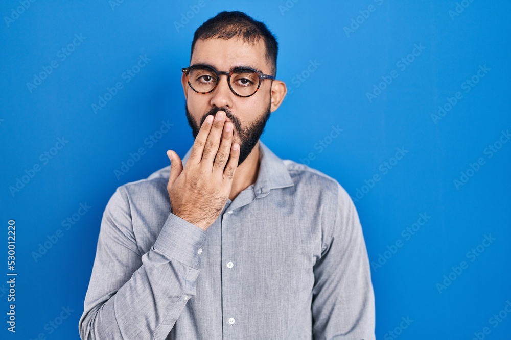 Middle east man with beard standing over blue background bored yawning tired covering mouth with hand. restless and sleepiness. Middle east man with beard standing over blue background bored yawning tired covering mouth with hand. restless and sleepiness.