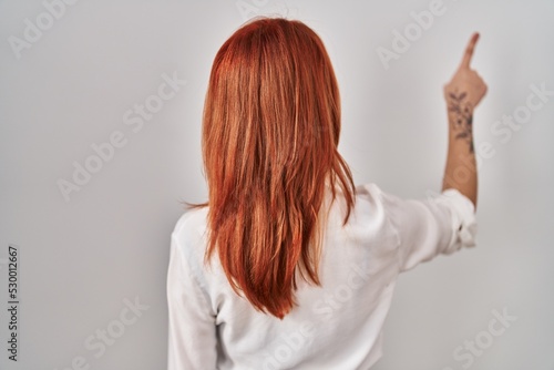 Young caucasian woman standing over isolated background posing backwards pointing ahead with finger hand