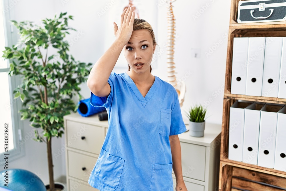 Young caucasian woman working at pain recovery clinic surprised with hand on head for mistake, remember error. forgot, bad memory concept. Young caucasian woman working at pain recovery clinic surprised with hand on head for mistake, remember error. forgot, bad memory concept.