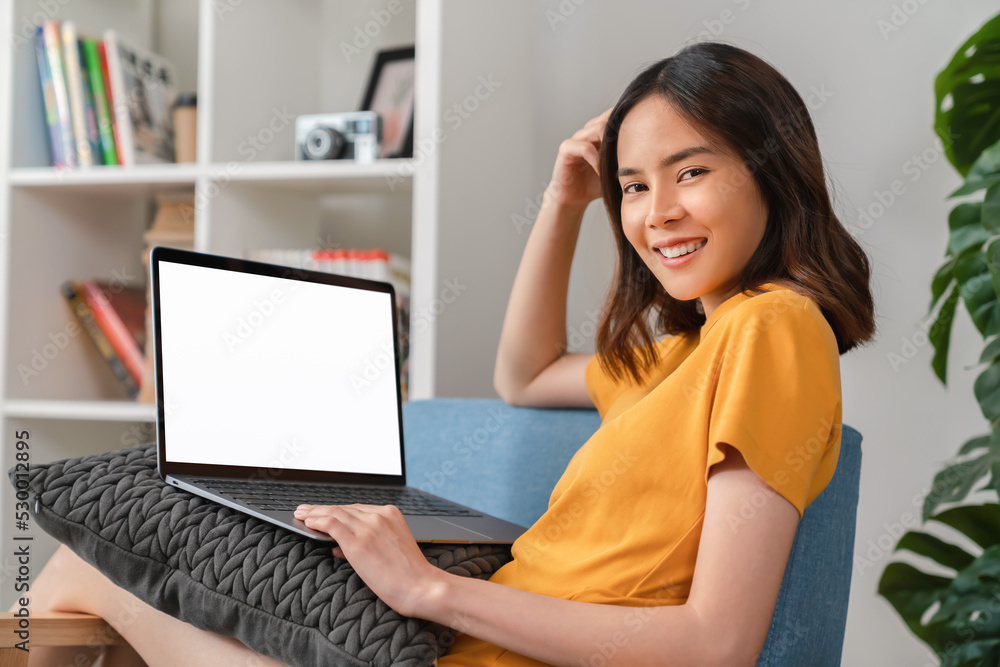 Naklejka premium Cheerful young woman wear orange shirt with sitting on sofa and using laptop computer at home.