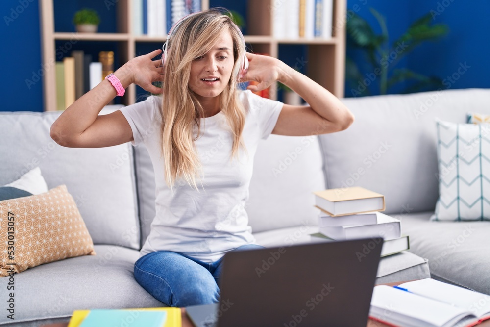 Young blonde woman studying using computer laptop at home trying to hear both hands on ear gesture, curious for gossip. hearing problem, deaf Young blonde woman studying using computer laptop at home trying to hear both hands on ear gesture, curious for gossip. hearing problem, deaf